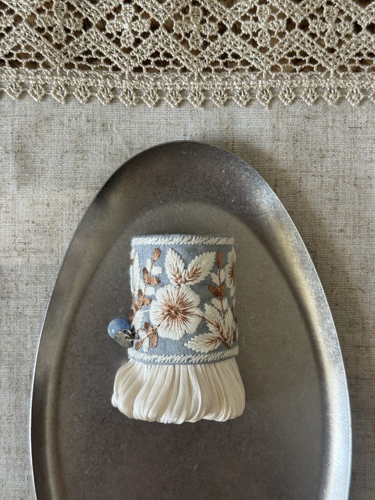 Front view of Bluebell Garden Pleat blue-gray floral hair cuff with ivory embroidery, pleats and a blue bead accent