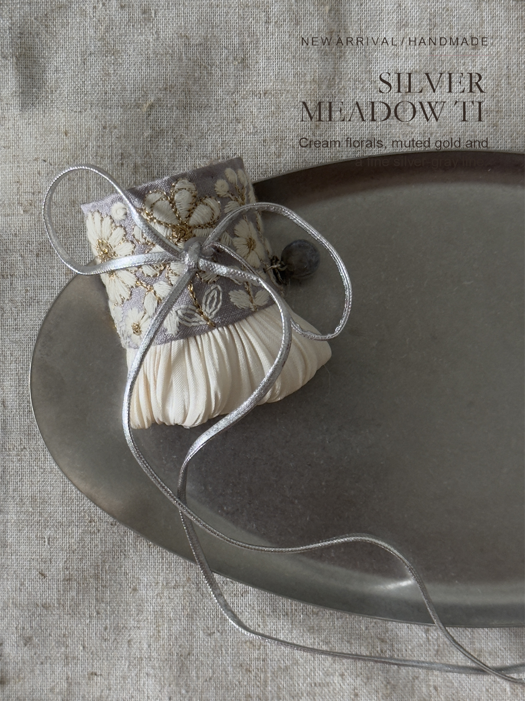 Silver Meadow Tie editorial still life with cream floral embroidery and ivory pleats