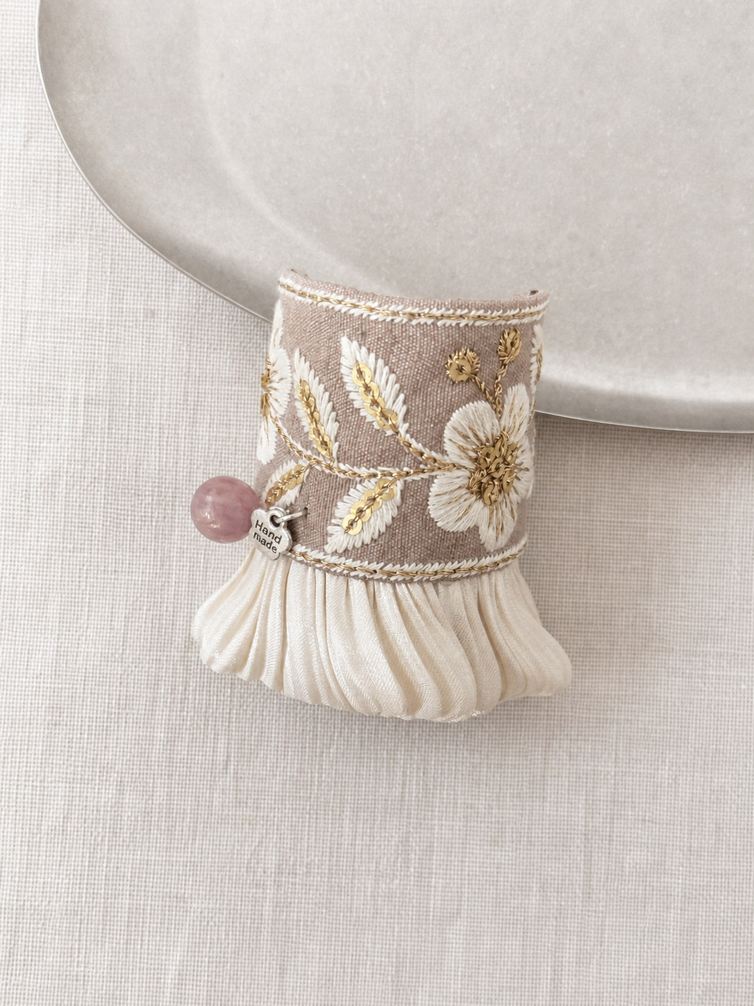 Close-up of cream floral embroidery and plum bead accent
